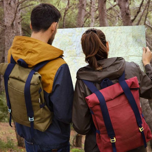 couple looking at a map in the forest, they carry roll top backpacks made of recycled canvas